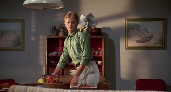 Movie still from “Matinee” (1993), directed by Joe Dante – A man standing at a table in a room; Medium shot, Low angle