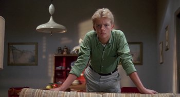 Movie still from “Matinee” (1993), directed by Joe Dante – A young man leaning over a couch in a living room; Medium shot, Low angle