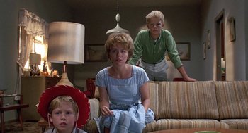 Movie still from “Matinee” (1993), directed by Joe Dante – A woman sitting on top of a couch next to a boy; Medium shot, Low angle