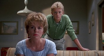 Movie still from “Matinee” (1993), directed by Joe Dante – A woman and a boy standing next to each other in a room; Medium shot, Low angle