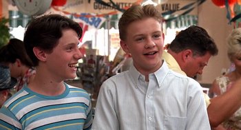 Movie still from “Matinee” (1993), directed by Joe Dante – Two young men standing next to each other in a market; Medium shot, Low angle