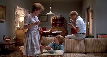 Movie still from “Matinee” (1993), directed by Joe Dante – A woman and two men sitting on a couch eating food; Wide shot, High angle