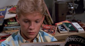 Movie still from “Matinee” (1993), directed by Joe Dante – A young boy reading a book in a room full of books; Close Up shot, High angle