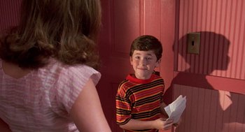 Movie still from “Matinee” (1993), directed by Joe Dante – A young boy holding an envelope in front of a woman; Medium shot, High angle