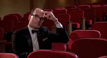 Movie still from “Matinee” (1993), directed by Joe Dante – A man in a suit and bow tie sitting in a theater; Medium shot, Low angle