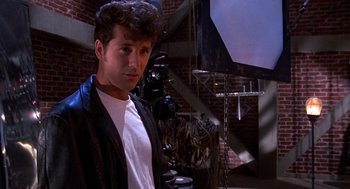 Movie still from “Matinee” (1993), directed by Joe Dante – A man in a black jacket standing in front of a brick wall; Medium shot, Low angle
