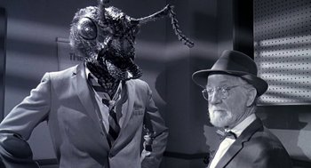 Movie still from “Matinee” (1993), directed by Joe Dante – A man wearing a suit and tie next to a man wearing a hat and glasses; Close Up shot, Over the shoulder angle