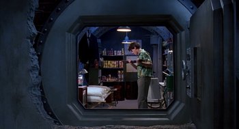 Movie still from “Matinee” (1993), directed by Joe Dante – A man standing inside of a room looking at his phone; Wide shot, High angle