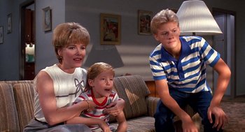 Movie still from “Matinee” (1993), directed by Joe Dante – A woman and two young boys sitting on a couch; Medium shot, High angle