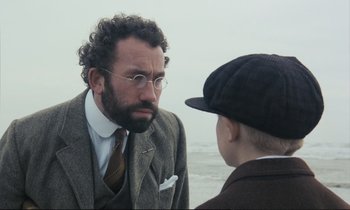 Movie still from “Maurice” (1987), directed by James Ivory – A man in a suit and tie talking to a boy in a hat; Close Up shot, Over the shoulder angle