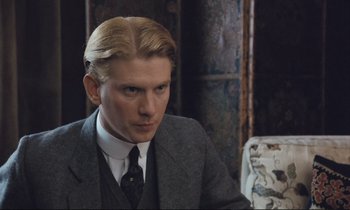 Movie still from “Maurice” (1987), directed by James Ivory – A man in a suit and tie sitting in front of a chair; Close Up shot, High angle