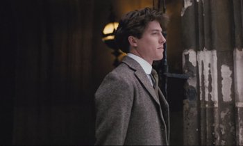 Movie still from “Maurice” (1987), directed by James Ivory – A man in a suit and tie standing in front of a building; Medium shot, Low angle