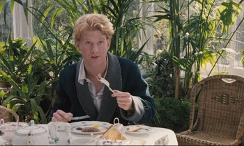 Movie still from “Maurice” (1987), directed by James Ivory – A man sitting at a table with a plate of food in front of him; Medium shot, High angle