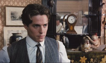Movie still from “Maurice” (1987), directed by James Ivory – A man in a suit and tie standing in front of a clock; Close Up shot, Over the shoulder angle