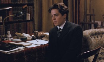 Movie still from “Maurice” (1987), directed by James Ivory – A man in a suit sitting at a table with papers; Medium shot, Over the shoulder angle