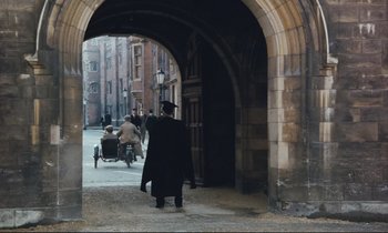 Movie still from “Maurice” (1987), directed by James Ivory – A man walking down a street under an archway; Extreme Wide shot, High angle