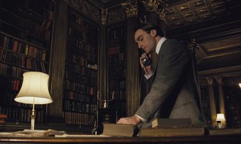 Movie still from “Maurice” (1987), directed by James Ivory – A man standing at a desk talking on a phone; Medium shot, Low angle