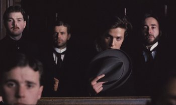 Movie still from “Maurice” (1987), directed by James Ivory – A man in a black suit and a man in a black suit and a man in a black suit and a man in a black hat; Close Up shot, Over the shoulder angle