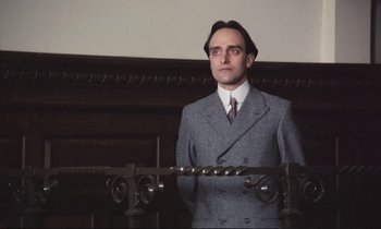Movie still from “Maurice” (1987), directed by James Ivory – A man in a suit and tie standing in front of a wall; Close Up shot, Low angle
