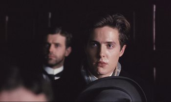 Movie still from “Maurice” (1987), directed by James Ivory – A man in a suit and tie standing next to another man in a suit and tie; Close Up shot, Over the shoulder angle