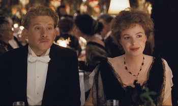 Movie still from “Maurice” (1987), directed by James Ivory – A man and a woman sitting at a table in front of a crowd; Close Up shot, High angle