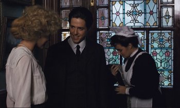 Movie still from “Maurice” (1987), directed by James Ivory – A group of people standing next to each other in front of a stained glass window; Medium shot, Over the shoulder angle