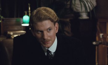 Movie still from “Maurice” (1987), directed by James Ivory – A man with blonde hair and a beard wearing a suit and tie; Close Up shot, Over the shoulder angle