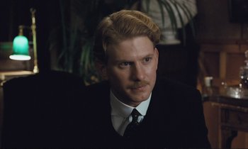 Movie still from “Maurice” (1987), directed by James Ivory – A man in a black suit and white shirt with blonde hair; Close Up shot, Over the shoulder angle