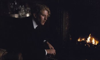 Movie still from “Maurice” (1987), directed by James Ivory – A man sitting in front of a fire place; Medium shot, Low angle