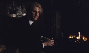 Movie still from “Maurice” (1987), directed by James Ivory – A man wearing a suit and tie in a dark room; Medium shot, Low angle