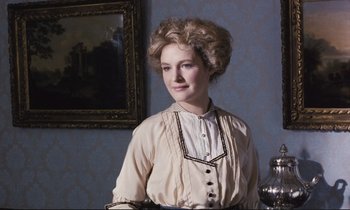 Movie still from “Maurice” (1987), directed by James Ivory – A woman in a white dress standing in front of a painting; Medium shot, Low angle