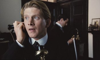 Movie still from “Maurice” (1987), directed by James Ivory – A man talking on a phone in front of another man; Close Up shot, Low angle