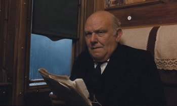Movie still from “Maurice” (1987), directed by James Ivory – An older man sitting on a train holding a newspaper; Close Up shot, Low angle