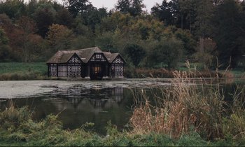 Movie still from “Maurice” (1987), directed by James Ivory – A house sitting next to a body of water; Extreme Wide shot, High angle