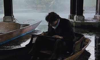 Movie still from “Maurice” (1987), directed by James Ivory – A man sitting in a boat writing on a paper; Medium shot, High angle