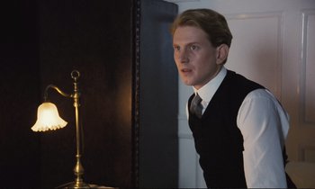 Movie still from “Maurice” (1987), directed by James Ivory – A man in a vest and tie standing in front of a mirror; Medium shot, Low angle