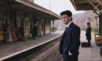 Movie still from “Maurice” (1987), directed by James Ivory – A man in a suit standing on a train platform; Medium shot, Low angle