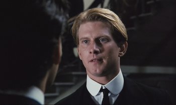 Movie still from “Maurice” (1987), directed by James Ivory – A man in a suit and tie looking at the camera; Close Up shot, Over the shoulder angle