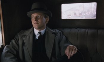 Movie still from “Maurice” (1987), directed by James Ivory – A man sitting in the back of a car wearing a hat; Medium shot, Low angle