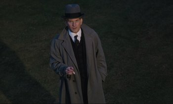 Movie still from “Maurice” (1987), directed by James Ivory – A man in a hat and a coat standing in a field; Medium shot, High angle