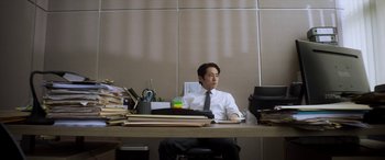 Movie still from “Mayhem” (2017), directed by Joe Lynch – A man sitting at a desk in front of a laptop computer; Medium shot, High angle