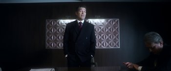 Movie still from “Mayhem” (2017), directed by Joe Lynch – A man in a suit standing in front of a table; Medium shot, Low angle