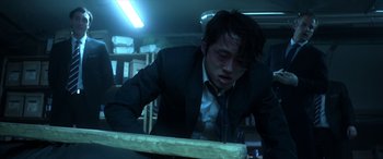 Movie still from “Mayhem” (2017), directed by Joe Lynch – A man in a suit and tie leaning over a table; Medium shot, Low angle
