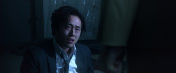 Movie still from “Mayhem” (2017), directed by Joe Lynch – A man in a suit and tie sitting in a dark room; Close Up shot, Over the shoulder angle