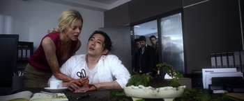 Movie still from “Mayhem” (2017), directed by Joe Lynch – A man sitting at a table in front of other people; Medium shot, Low angle