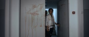 Movie still from “Mayhem” (2017), directed by Joe Lynch – A man in a white shirt is walking in a room with blood all over it; Medium shot, Low angle