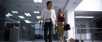 Movie still from “Mayhem” (2017), directed by Joe Lynch – A man and a woman holding hands while walking down a hall way; Wide shot, Low angle