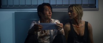 Movie still from “Mayhem” (2017), directed by Joe Lynch – A man and a woman sitting next to each other holding a piece of paper; Close Up shot, Low angle