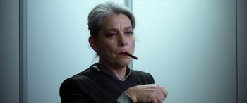 Movie still from “Mayhem” (2017), directed by Joe Lynch – An older woman smoking a cigarette while looking at the camera; Close Up shot, Over the shoulder angle