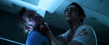 Movie still from “Mayhem” (2017), directed by Joe Lynch – A man with a knife in his mouth and a man with a tie in his neck; Close Up shot, Low angle